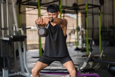 Spor salonunda kettlebell egzersizi yapan bir adam, fonksiyonel fitness ve kuvvet eğitimine önem verir..