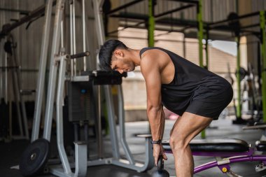 Spor salonunda kettlebell egzersizleri yapan odaklanmış genç bir adam fitness ve güç eğitimine olan bağlılığını gösteriyor..