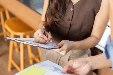 Bir iş kadını, çağdaş bir ofis ortamında bir meslektaşıyla işbirliği yaparken notlar alır ve belgeleri imzalar..