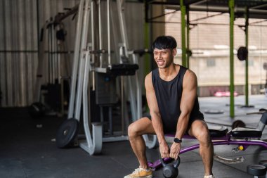 Odaklanmış bir çaydanlık çanı egzersizi yapan genç bir adam spor salonundaki dayanıklılık eğitimini ve fitness bağlılığını vurguluyor..