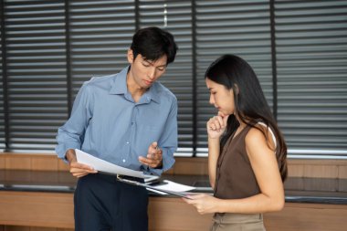 Genç bir adam ve kadın, şık bir ofis ortamında önemli proje belgelerini tartışıyor, takım çalışması sergiliyorlar..