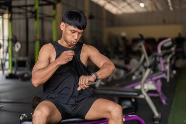 Spor salonunda odaklanmış bir adam, bir bankta oturmuş, spor ve teknolojiyi vurguluyor..