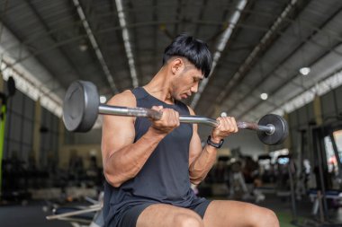 Genç bir adam, iyi donanımlı bir spor salonunda biseps kıvrımları için halter kaldırırken güç antrenmanına odaklanır..