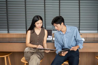 İki genç profesyonel belge inceleme ve görüşleri paylaşma, modern ofis ortamında işbirliği ve takım çalışmasını teşvik etme.