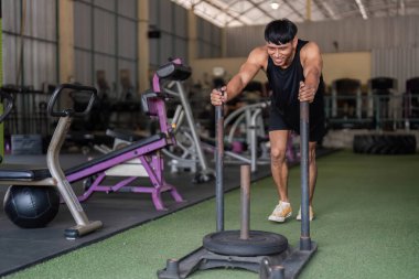 Odaklanmış bir adam modern bir spor salonunda kızak itme egzersizi yapar, fitness ve güç eğitimine kendini adamış olduğunu gösterir..