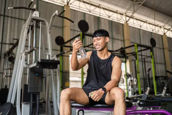 Bir adam spor yaptıktan sonra su şişesini zevkle inceler, vücut ve sağlıktaki susuzluğun önemini gösterir..