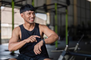 Spor salonunda gülümseyen bir adam. Akıllı hareketlerini kontrol ediyor. Formda ve sağlıklı bir yaşam sürüyor..