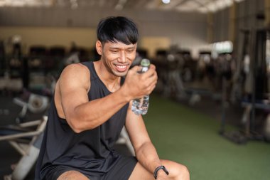 Spor salonunda su içerken gülümseyen bir adam formda olmanın önemini gösteriyor..