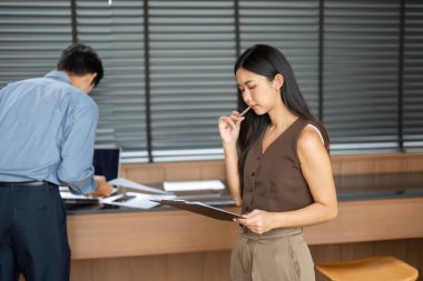 Bir iş kadını, modern bir ofis ortamında bir işadamı telefonla konuşurken düşünceli bir şekilde belgeleri gözden geçirir..