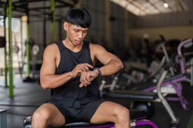 Spor salonunda genç bir adam egzersiz ölçümlerini kontrol ediyor, spor ve teknoloji entegrasyonunu vurguluyor..