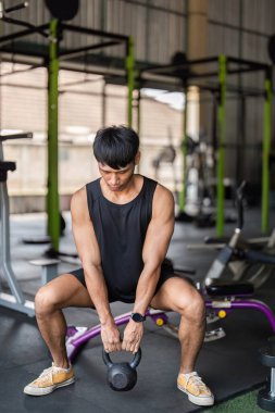 Kendini bir spor salonunda kettlebell egzersizi yapmaya adamış genç bir adam. Güç ve zindelik gösterisi yapıyor. Egzersiz rutinine ve fiziksel sağlığa odaklan.