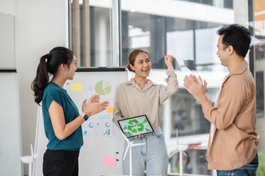 Çağdaş bir ofis ortamında sürdürülebilirlik ve ESG stratejileri üzerine başarılı bir sunumu kutlayan çeşitli profesyoneller takımı.