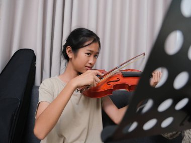 İki genç kız bir kanepede oturuyor, biri keman çalıyor. Diğer kız kemana dokunuyor, muhtemelen arkadaşına yardım ediyor. Arkadaşlık ve destek kavramı