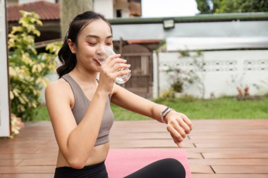 Yogadan sonra serinletici bir içecek içen bir kadın, vücut geliştirme rutinlerinde susuzluğun ve sağlığın önemini gösterir..