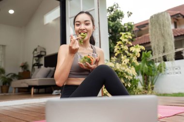 Yoga yapan ve sağlıklı bir salata yiyen bir kadın, refahı arttıran ve rahat bir evde dengeli bir yaşam süren bir kadın..