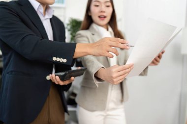 İki iş adamı stratejik bir tartışmaya giriştiler, proje belgelerini gözden geçiriyorlar ve parlak bir ofis ortamında işbirliği yapıyorlar..