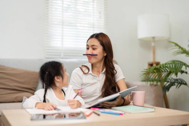 Bir anne ve kızın birlikte ev ödevi yaparken gülümsemeleri ve kahkahaları paylaşması ve öğrenmenin zevklerini göstermesi gibi eğlenceli bir etkileşim gerçekleşir..