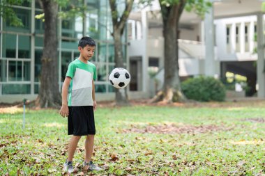 Genç bir çocuk topu havada tutarak futbol becerilerini çalışarak biraz boş zamanın tadını çıkarıyor. Ayar, açık hava egzersizinin ve sportmenliğin özünü yakalıyor..
