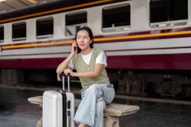 Genç bir kadın bir telefon görüşmesi yapıyor, tren istasyonunda beklerken endişelerini dile getiriyor, seyahatlerde iletişimin önemini gösteriyor..