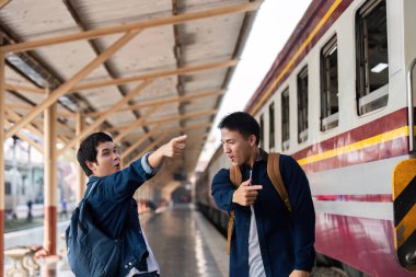 İki arkadaş hareketli bir şekilde seyahat planlarını tartışıyor ve yola çıkmadan önce tren istasyonunda coşkularını sergiliyorlar..