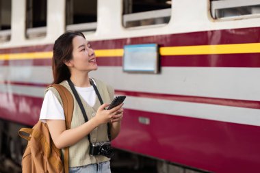 Bir gezgin telefonuna bakarken gülümsüyor, tren istasyonundaki macerasının heyecanını yakalıyor, keşfini ve seyahat şehvetini vurguluyor..