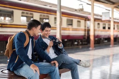 İki arkadaş tren istasyonunda bir bankta oturur, fotoğraflara bakarken bir ışık anı paylaşırlar. Kahkahaları seyahat ve keşiflerin neşesini somutlaştırıyor..