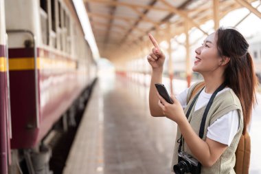 Neşeli bir ifadeyle, bir gezgin, tren istasyonunda bir anlık neşe ve spontanelik sergileyerek gelen treni işaret eder..