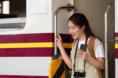 Kameralı ve akıllı telefonlu neşeli bir gezgin trenden iniyor, yeni hedefleri keşfetmek ve anılarını yakalamak için heyecanlı..