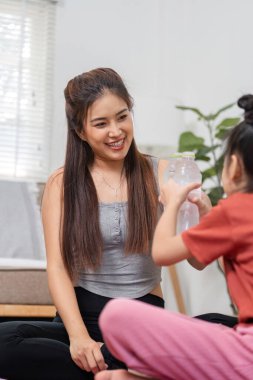 Bir anne, kızını etkileşimli bir fitness seansına dahil eder. Eğlence ve takım çalışmasını ön plana çıkarırken, sağlıklı alışkanlıkları teşvik eder..