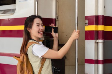 Macerasına hevesle hazır olan genç bir kadın telefonunu tren kapısında tutarken gülümsüyor, seyahat hevesini somutlaştırıyor..