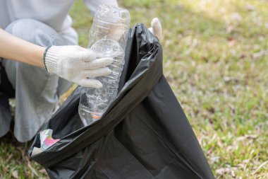 Eldiven takan biri plastik şişe toplar ve temizlik sırasında onları siyah bir çöp torbasına koyar..