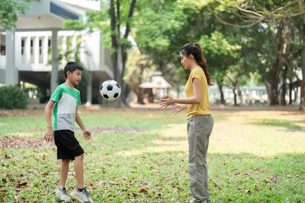 Genç bir erkek ve kız parkta birlikte futbol oynayarak eğleniyorlar. Takım çalışması ve arkadaşlıklarını gösteriyorlar. Açık hava aktivitelerinin tadını çıkarıyorlar..