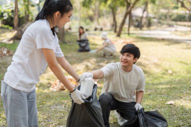 Genç bir gönüllü, bir park temizleme etkinliği sırasında bir çanta dolusu atığı takım arkadaşına teslim ediyor..