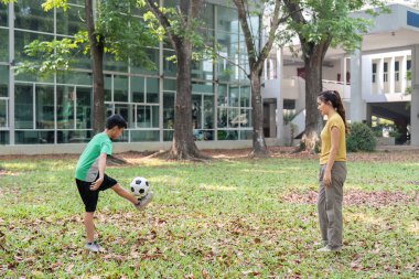 Genç bir çocuk, parkta antrenman yaparak futbol yeteneklerini sergiliyor. Annesi de onu cesaretlendiriyor..