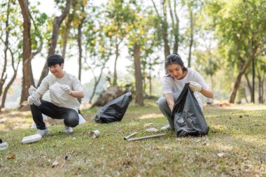 Gönüllüler parktaki çöpleri toplamakla meşgul olup, çevre dostu olma ve toplumsal katılıma bağlılıklarını vurguluyorlar..