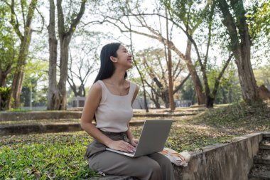 Bir kadın laptopunu açık havada ağaçlarla çevrili halde kullanılabilir eşyalarla sürdürülebilir bir yaşam tarzını desteklerken gülümsüyor..