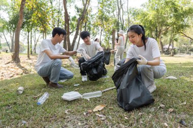 Bir grup gönüllü, takım çalışması ve çevre sorumluluğunu vurgulayarak parkta çeşitli atık eşyalar topluyor.