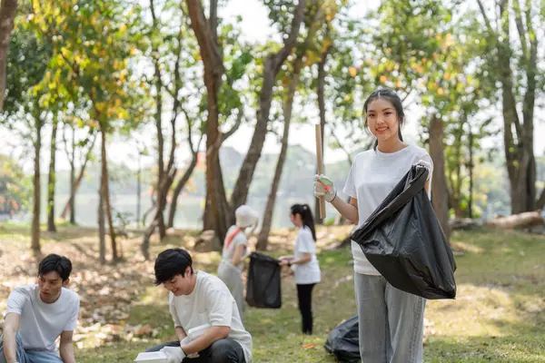 Bir grup hevesli gönüllü toplum temizliği yapıyor, çöp topluyor ve park ortamında sürdürülebilirliği destekliyor.