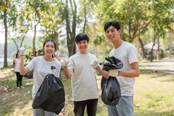 Toplum temizliği sırasında çöp torbalarını gururla tutan üç genç gönüllü, sürdürülebilirliğe olan bağlılıklarını vurguladı.