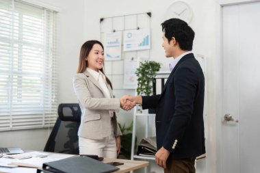 Finansal danışman ve müşteri, modern ofis ortamında başarılı bir anlaşma ve ortaklığı sembolize ederek el sıkışıyor..
