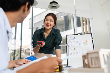 Gülümseyen bir kadın mimar modern bir ofiste bir meslektaşıyla görüşür, proje detayları ve sürdürülebilirliği tartışır..
