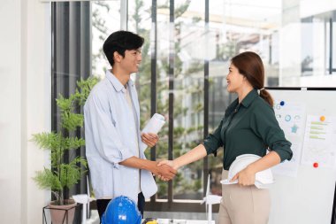 Mühendisler sürdürülebilir proje planlarını tartıştıktan sonra el sıkışıyor, işbirliği ve çevre sorumluluğunu vurguluyorlar.