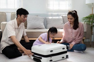 Bir anne, baba ve küçük kızları, aile seyahatine hazırlanmanın heyecanını vurgulamak için evde eğlenceli bir toplanma seansına katılıyorlar. Görüntü kahkaha ve beraberliği yakalar..