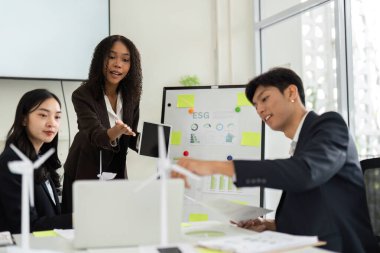 Çeşitli bir ekip, şirket sürdürülebilirliğini ve çevre dostu uygulamaları geliştirme amaçlı yenilikçi ESG girişimlerini tartışmak üzere bir konferans odasında işbirliği yapıyor..