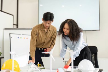 İki profesyonel, yenilenebilir teknoloji modelleri ve dizüstü bilgisayarlarla ilgilenerek, işyerinde sürdürülebilir çözümler üreten bir ortaklığı örnek gösteriyorlar..