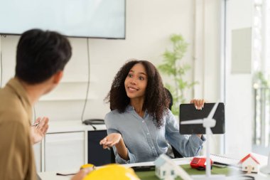 İki profesyonel, yenilenebilir enerji ve konut kavramlarını göstermek için modeller kullanarak sürdürülebilir kalkınma fikirleri üzerinde dinamik bir şekilde etkileşim halindedir..