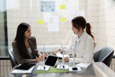 ESG stratejileri hakkında fikir ve görüşleri paylaşan iki kadın, şirketlerinde sürdürülebilirlik çabalarını artırmak için rüzgar enerjisi modellerini inceliyor.