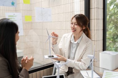 Bir profesyonel, sürdürülebilir enerji çözümlerini tartışırken, ESG 'de etkili iletişimin özünü yakalayan rüzgar türbini modellerini hevesle sunuyor.