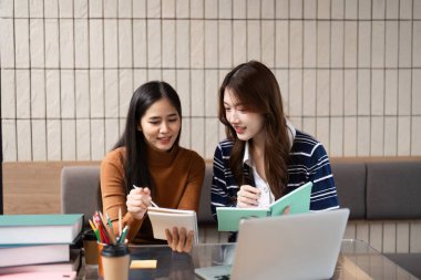 Canlı bir kafe ortamında, iki öğrenci hevesle materyallerini gözden geçirir ve çalışma notları üzerinde fikir alışverişinde bulunurlar..