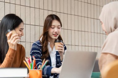 Dost canlısı bir kafe ortamında, üç öğrenci kahvelerini içerken çalışmaları hakkında tartışmalara girerek, destekleyici bir akademik atmosferi yansıtıyor..